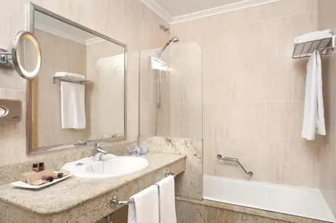 Baño con lavabo, espejo de aumento y bañera con mampara en el Hotel Talaso Atlántico