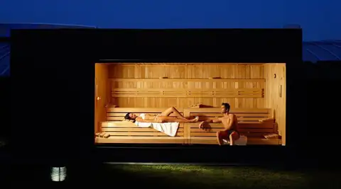 Sauna de madera iluminada vista desde el exterior por la noche en Termaria Casa del Agua