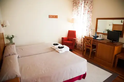 Habitación con dos camas, butaca roja y escritorio en el hotel de Termas de Cuntis