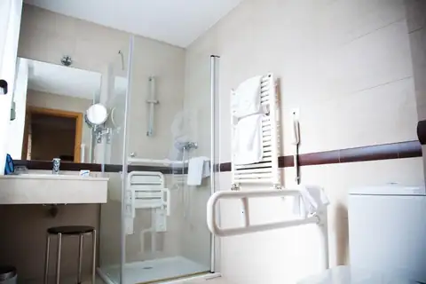 Baño adaptado con ducha a ras de suelo, asiento abatible y barras de apoyo en Termas de Cuntis