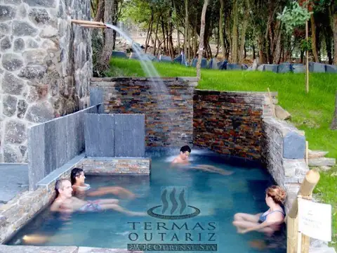 Bañistas en una poza termal de piedra con caño de agua en Termas Outariz