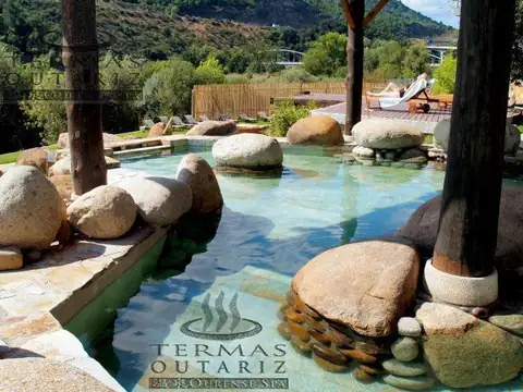 Piscina termal entre grandes rocas de granito y troncos de madera en Termas Outariz