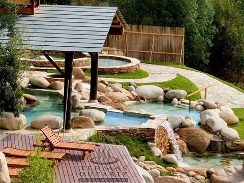 Pozas termales con rocas, pérgola de madera y tumbonas en los jardines de Termas Outariz