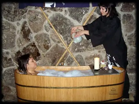 Baño en tina de madera con espuma y terapeuta vertiendo agua en Termas Outariz