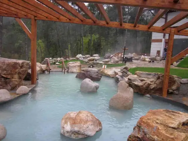 Piscina termal exterior entre rocas y pérgola de madera en las Termas de Prexigueiro, en Ribadavia